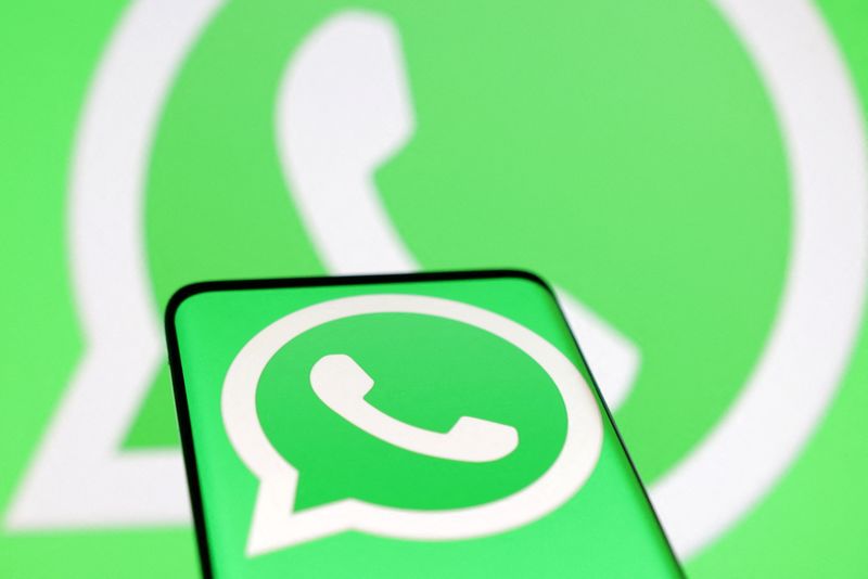 A close-up of the WhatsApp logo on a smartphone screen against a larger WhatsApp background, representing the platform at the center of an EU investigation into Meta's ban on rival AI chatbots.